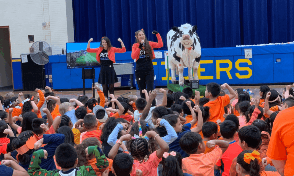 Carly the cow with PETA TeachKind Staffers, and students holding their arms up in a strong pose