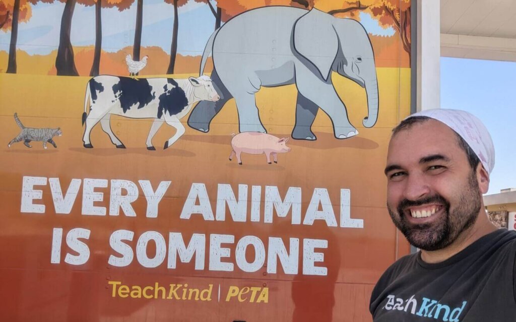 Robbie smiles in front of the TeachKind truck that reads "every animal is someone"