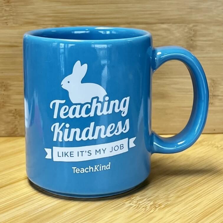 Blue TeachKind mug with a white rabbit cartoon that reads "TeachKind Kindness Like It's My Job" TeachKind