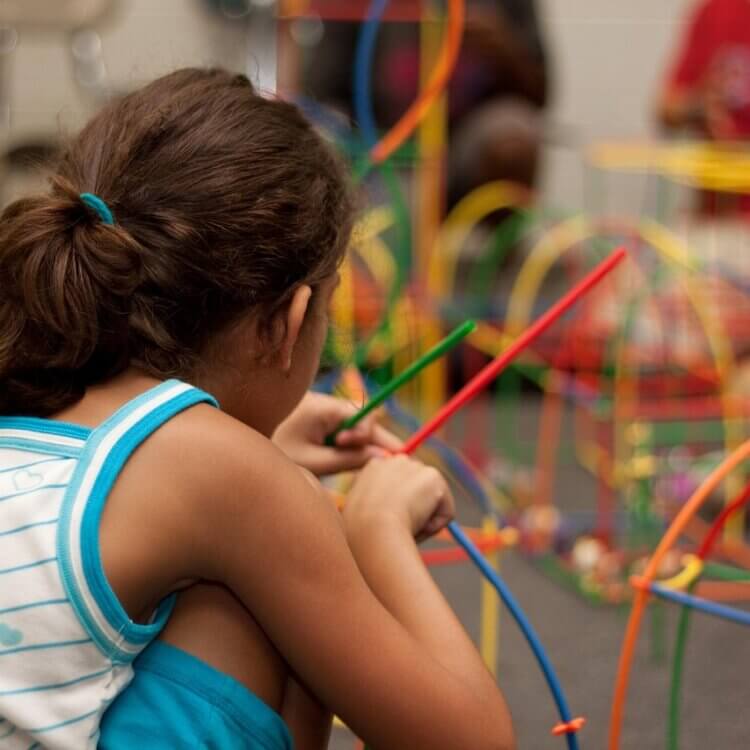 A young girl builds a structure with colorful, bendable sticks