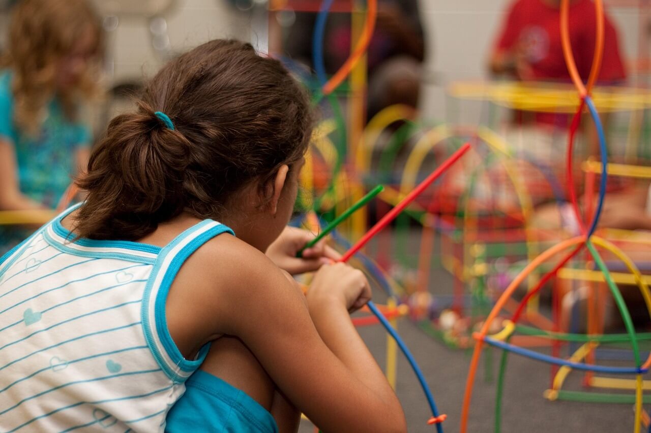 A young girl builds a structure with colorful, bendable sticks