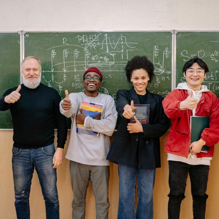 Students and a teacher stand together, giving a thumbs up in front of a chalkboard