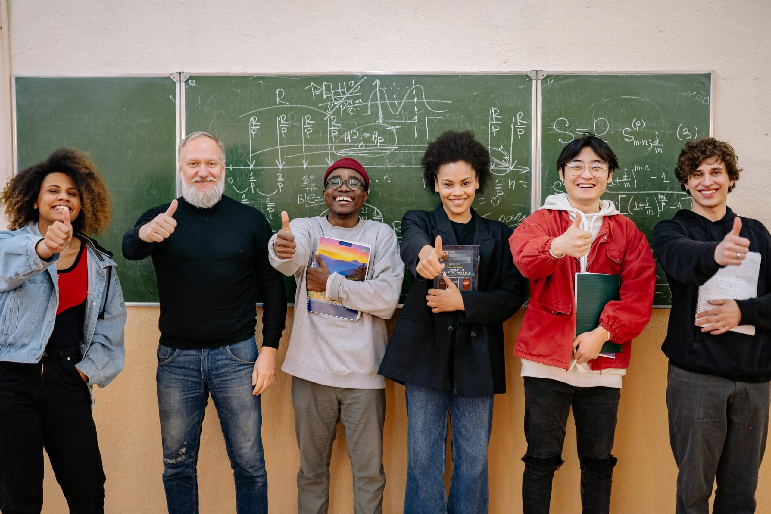 Students and a teacher stand together, giving a thumbs up in front of a chalkboard