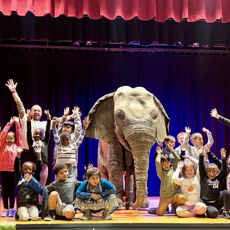 Students celebrate with their hands in the air next to Ellie, the animatronic elephant