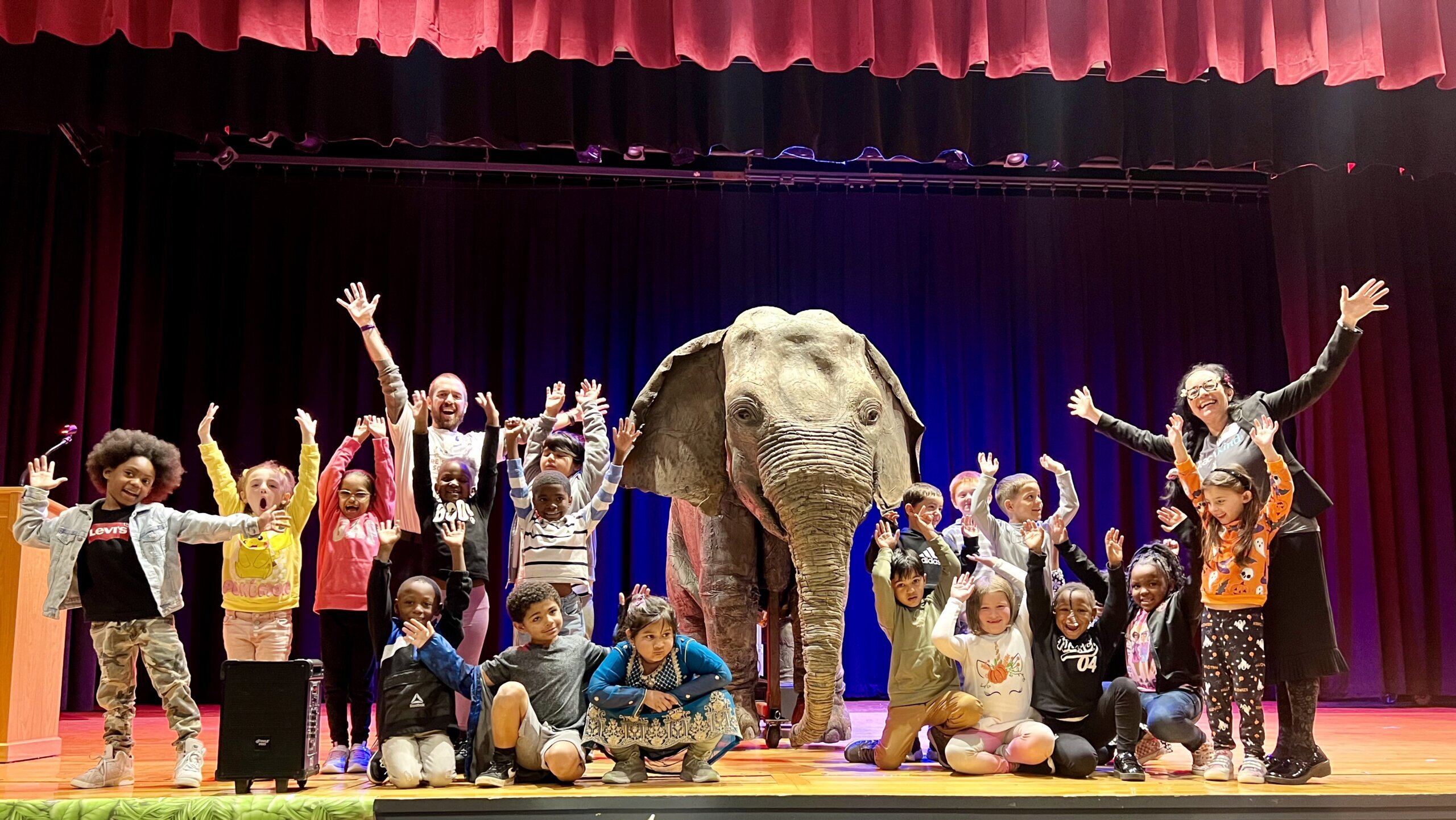 Students celebrate with their hands in the air next to Ellie, the animatronic elephant