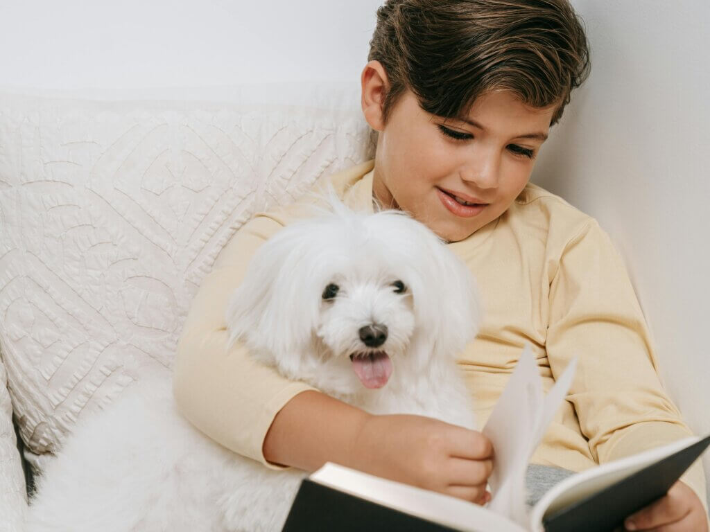 kid sitting with a dog, reading a book