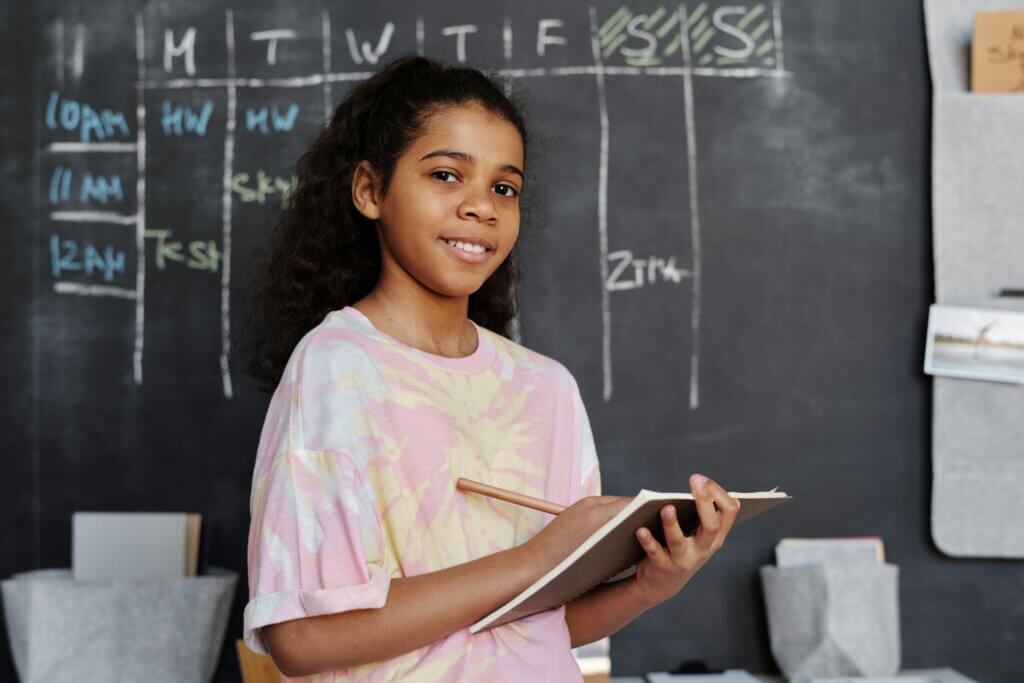 Gril in Pink Crew Neck T-shirt Holding Notepad in front of a chalkboard