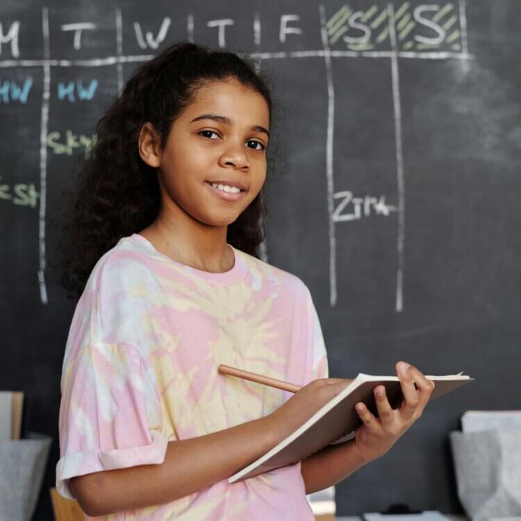 Gril in Pink Crew Neck T-shirt Holding Notepad in front of a chalkboard