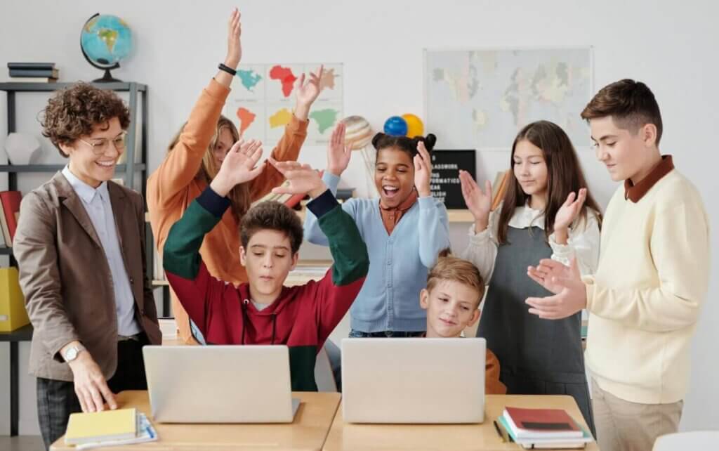 A group of students gathered around two laptops, celebrating, smiling, and clapping.
