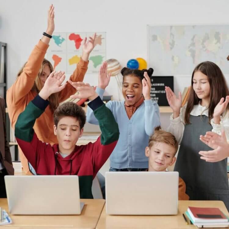 A group of students gathered around two laptops, celebrating, smiling, and clapping.