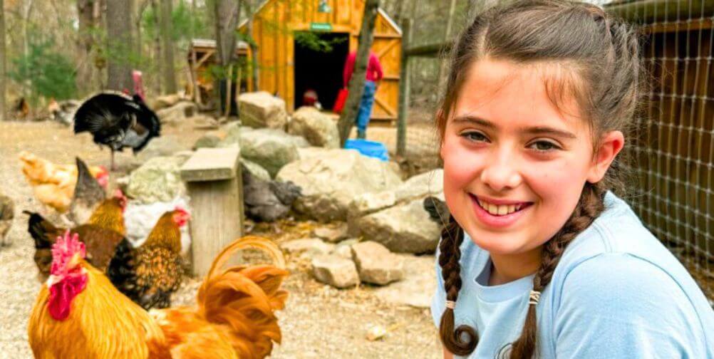 Kind kid, Dani, smiling with chickens and a turkey at an accredited sanctuary