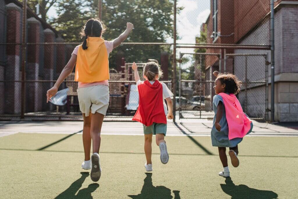 Children wearing capes run joyfully on a sunny day, embracing imaginative play and outdoor fun