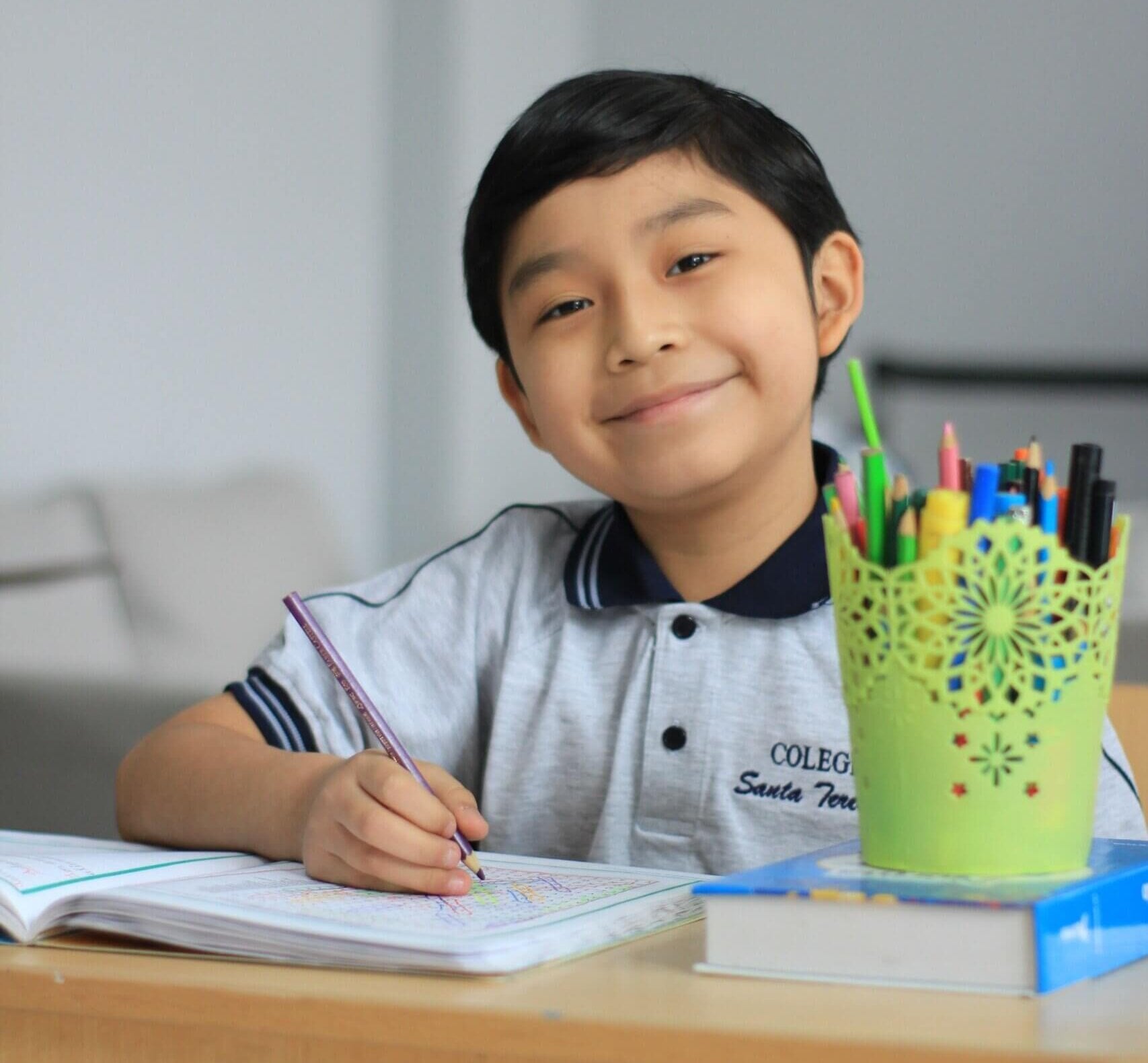 A young student sitting at a desk with a notebook and assorted pencils