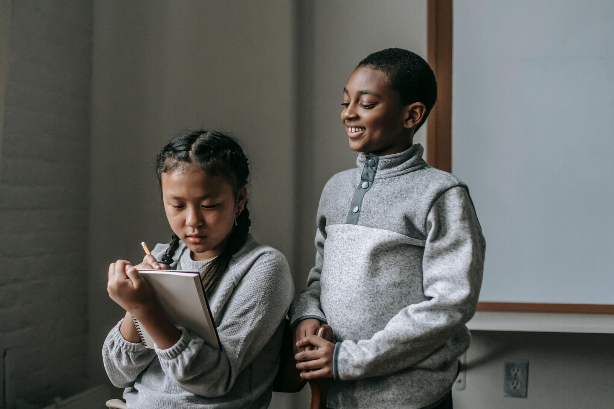 Two children engaged in a classroom activity, one smiling and the other taking notes.