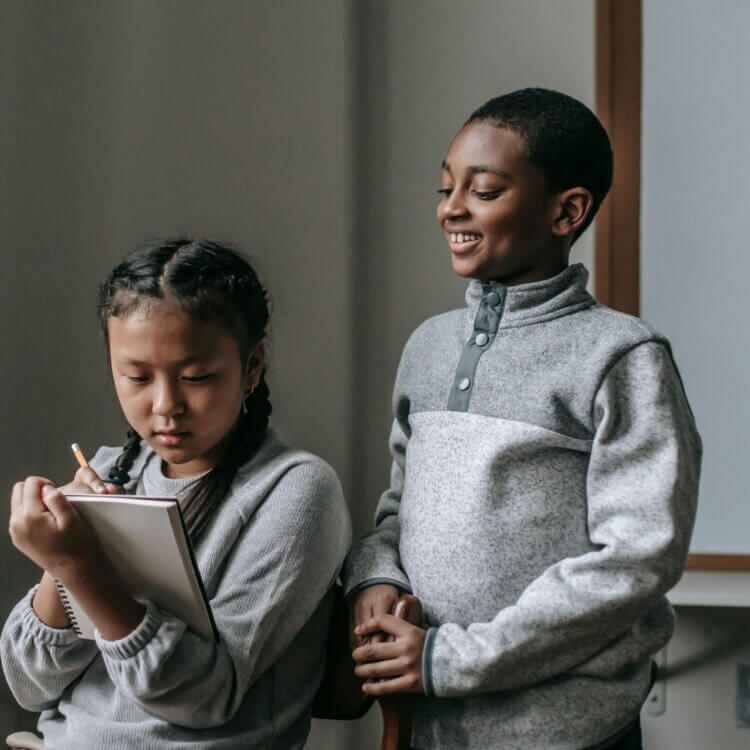 Two children engaged in a classroom activity, one smiling and the other taking notes.