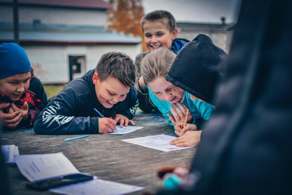 Smiling students working together outdoors on a wooden table, fostering creativity and teamwork.