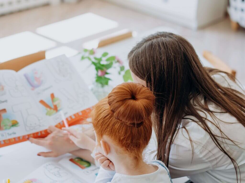 A woman helps her daughter with homework at a desk, emphasizing education and bonding.