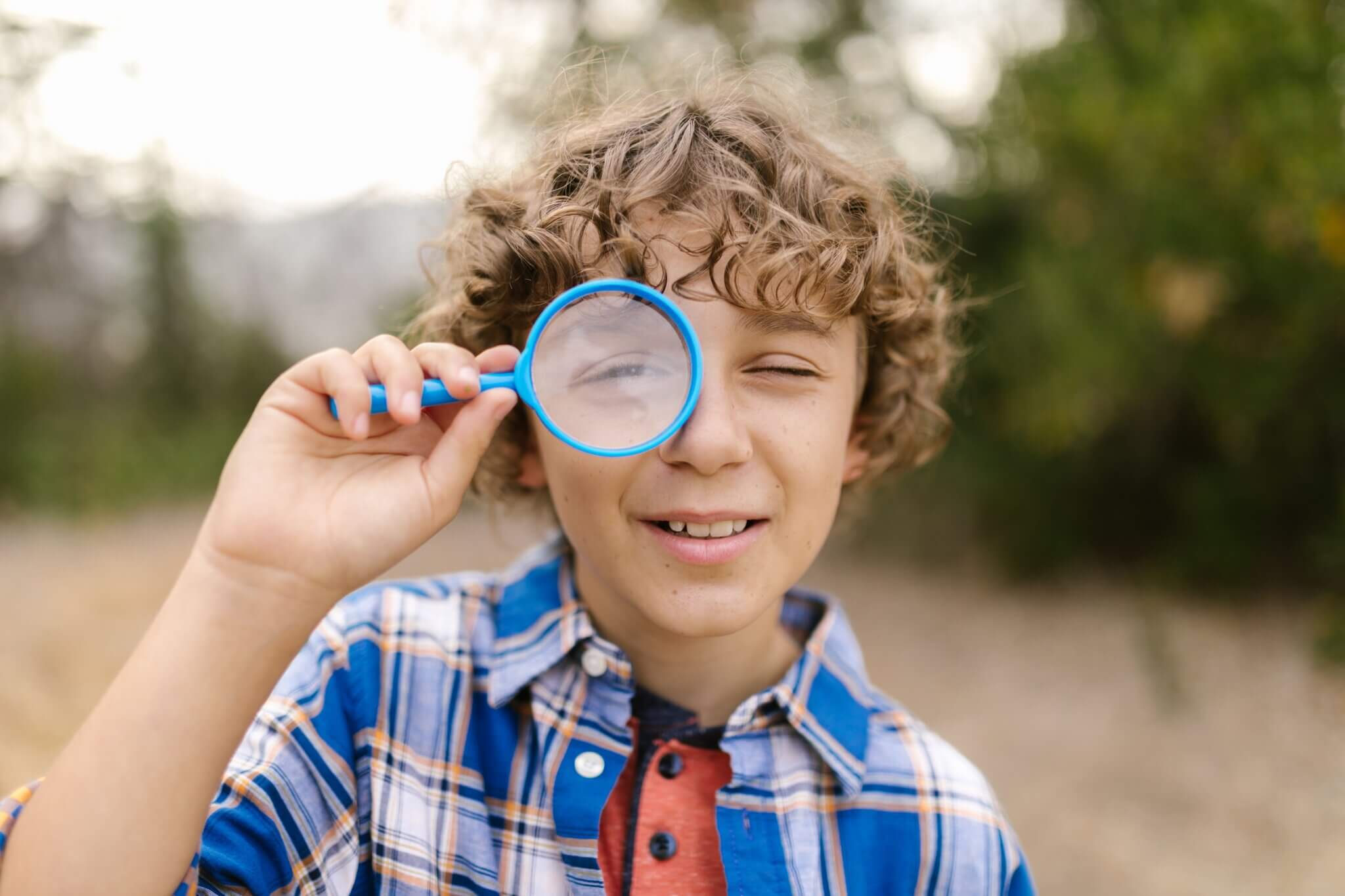 A happy child with curly hair looking through a magnifying glass in a playful outdoor setting