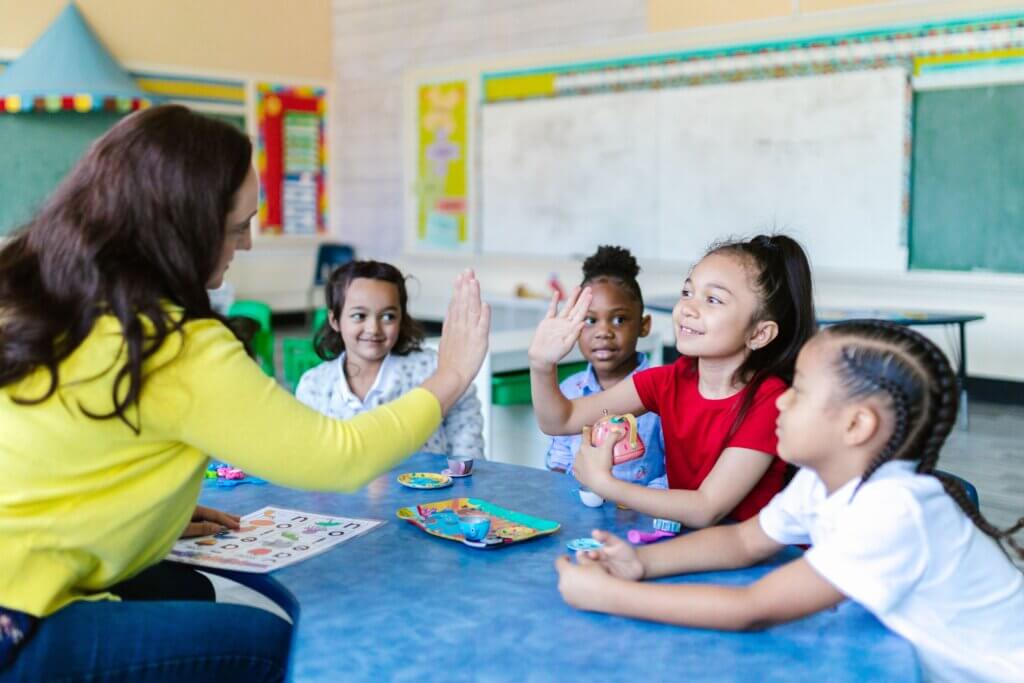 Teacher and diverse students high-five in a lively classroom setting