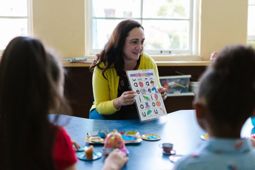 A teacher engaging young children in a fun learning activity with a phonics chart in a classroom setting.