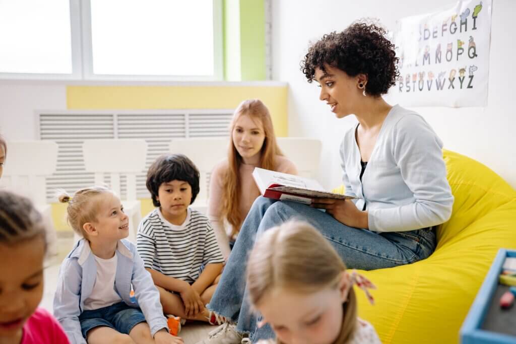 A teacher reading to young students in a colorful classroom setting.