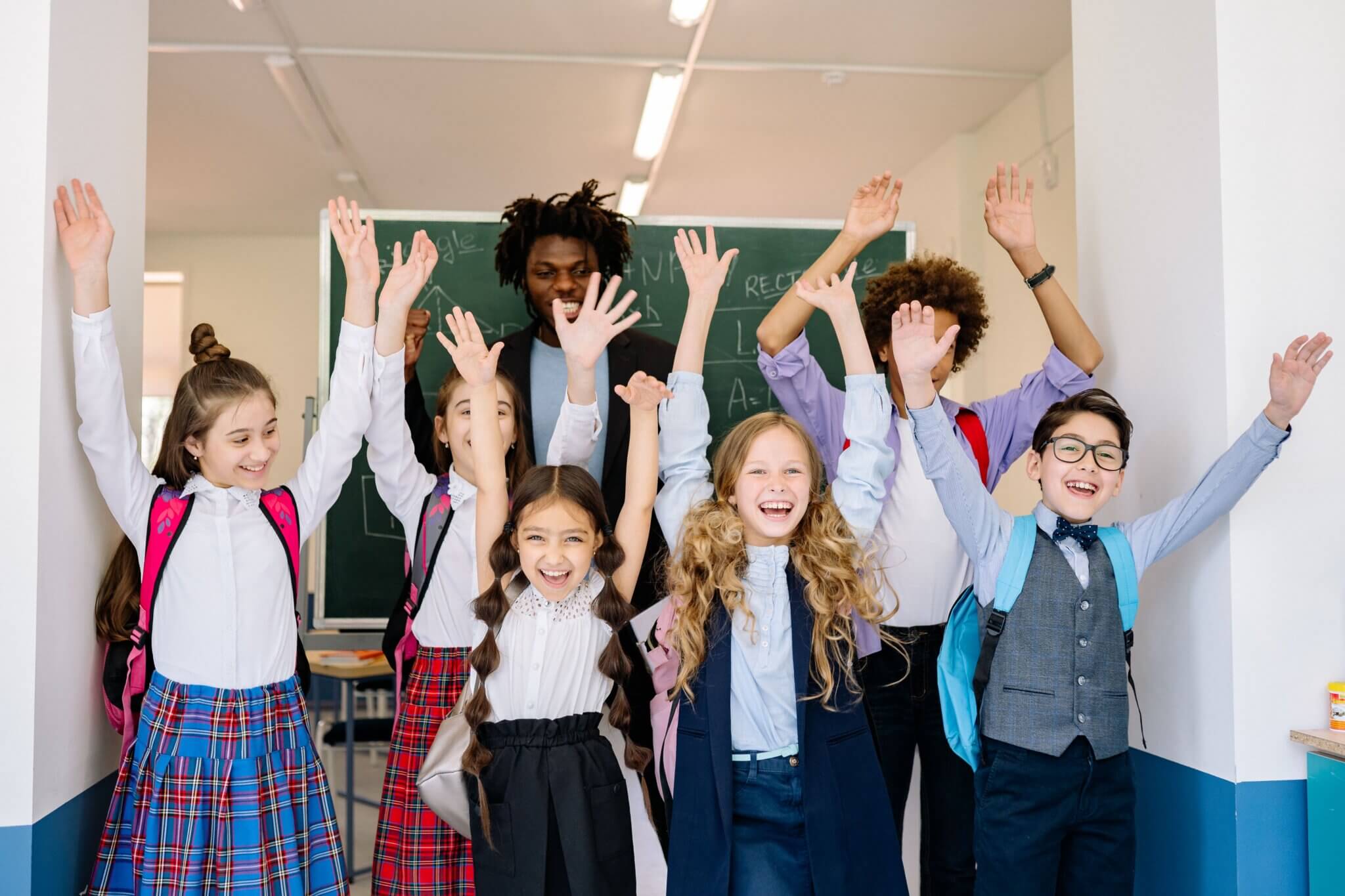 Joyful group of school children raising their hands in an indoor classroom setting