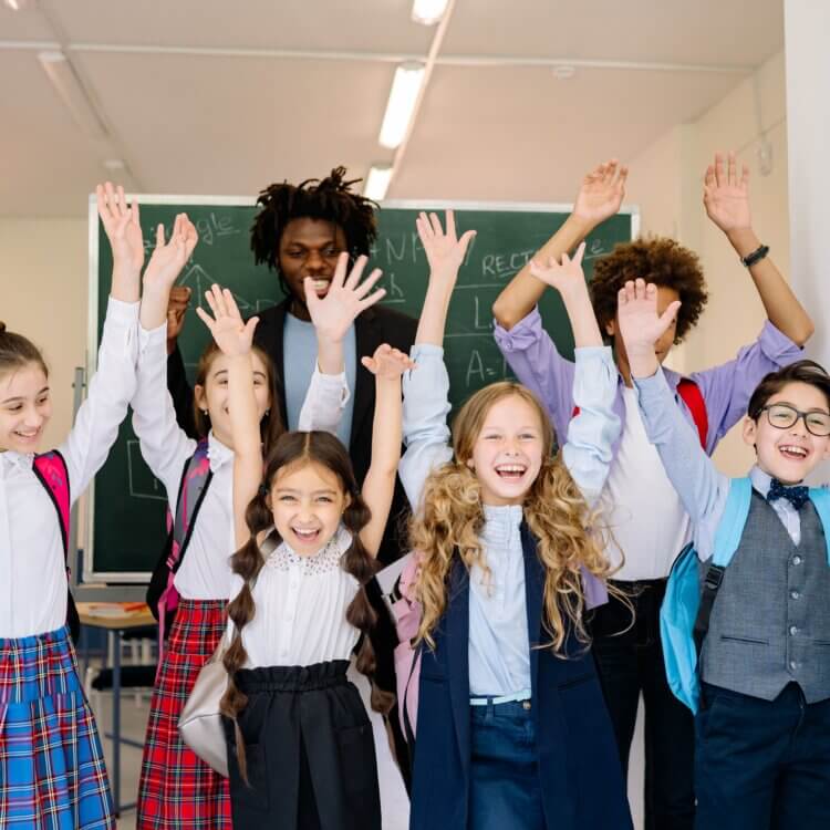 Joyful group of school children raising their hands in an indoor classroom setting