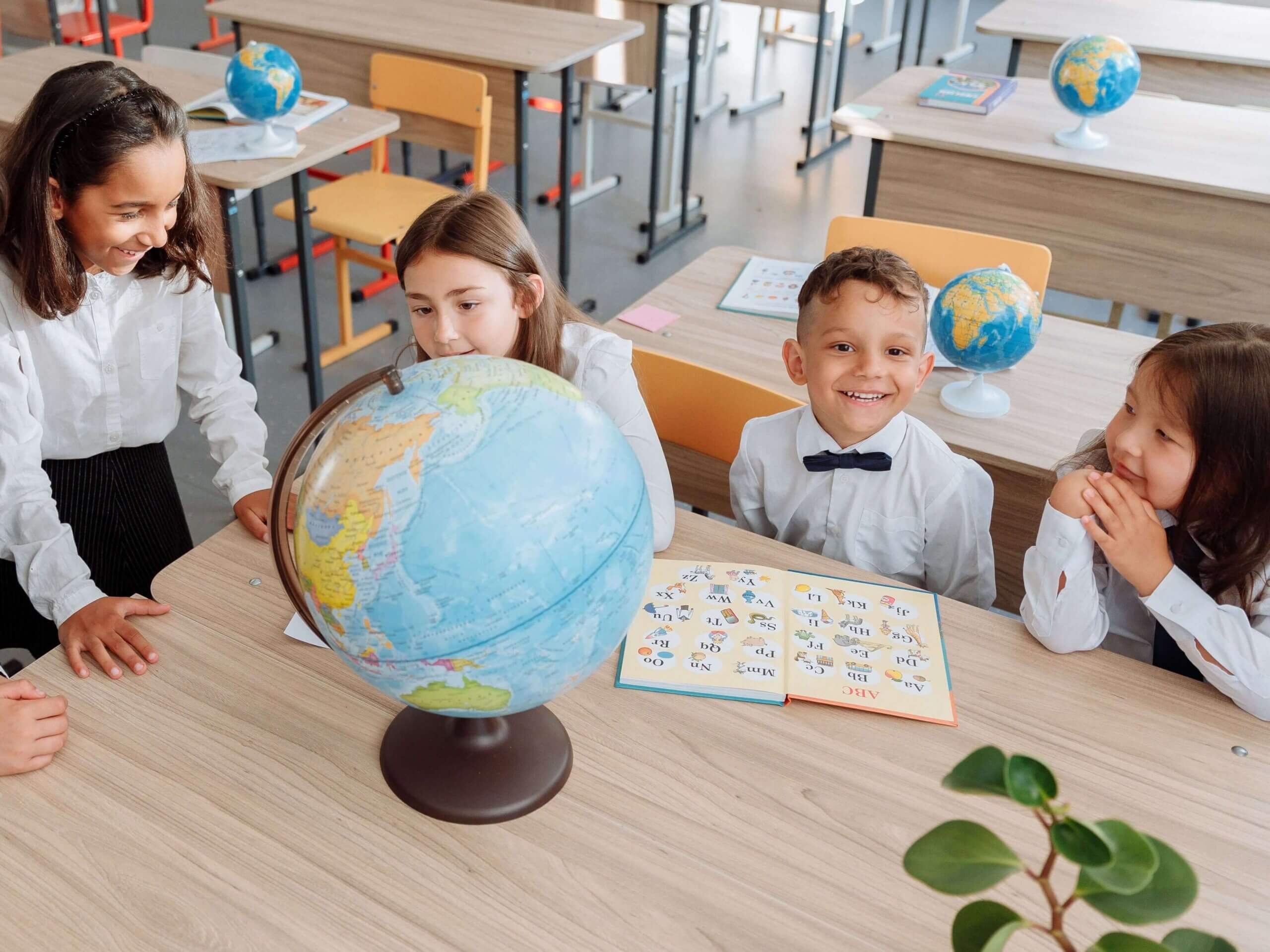 Group of children learning about geography using a globe in a bright classroom setting