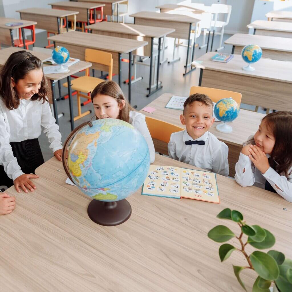 Group of children learning about geography using a globe in a bright classroom setting