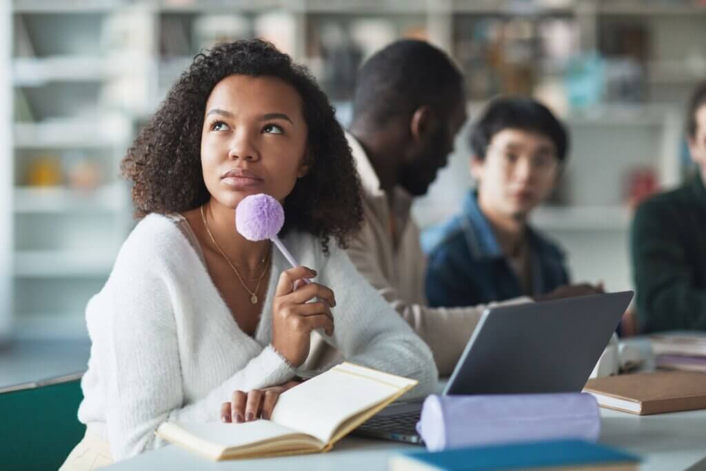 Student thinking in class with book and pen